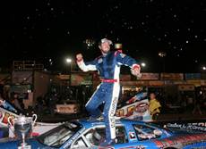 A man standing on top of a car in the middle of a race track.