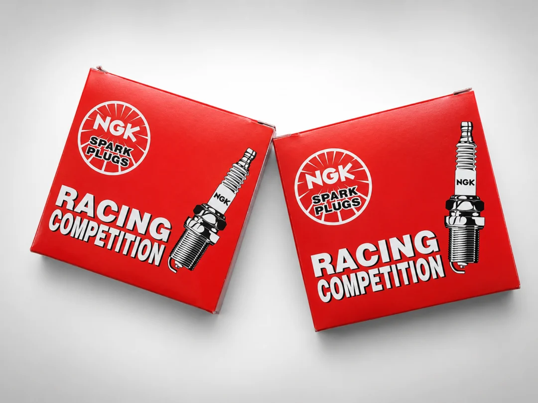 Two red boxes with the words "NGK Racing Competition" printed on them, sitting on a white surface